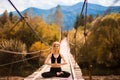 Woman meditating in lotus position on bridge over mountain river in forest Royalty Free Stock Photo