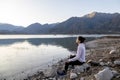 Woman meditating on the shore of a lake while enjoying the nature landscape. Royalty Free Stock Photo
