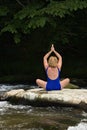 Woman meditating with yoga on a flat river rock.