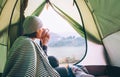 Woman meets cold morning sitting in touristic tent with cup of hot tea. Active vacation concept image. Royalty Free Stock Photo