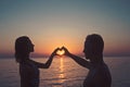 Woman and man with heart hands at sea water in sunset. Summer holidays and travel vacation. Family and valentines day Royalty Free Stock Photo