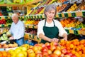 Woman merchandiser in apron putting goods on shelf in supermarket