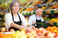 Woman merchandiser in apron putting goods on shelf in supermarket