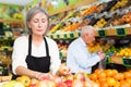 Woman merchandiser in apron putting goods on shelf in supermarket