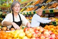 Woman merchandiser in apron putting goods on shelf in supermarket