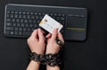 Woman with metal chain holding credit card over keyboard, online shopping addiction concept