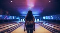 a woman in mid-throw as she releases the bowling ball down the lane, viewed from behind. The composition conveys the Royalty Free Stock Photo