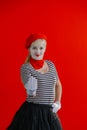 Woman mime near a red wall in a red beret shows a sign with her hand.