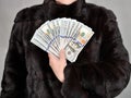 A woman in a mink coat holds many hundred dollar bills in her hands. Front view. Studio shot Royalty Free Stock Photo