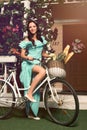 Woman in mint dress standing with bicycle near her house