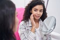 Woman with mirror in hand touches cheek with right hand Royalty Free Stock Photo