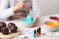 Woman mixing cream with light blue food coloring at white wooden table, closeup. Decorate cupcakes