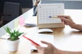 Woman with mobile phone in her hands pointing with pen to date on desk calendar closeup Royalty Free Stock Photo