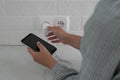Woman with mobile phone plugging charger in socket on white brick wall, closeup