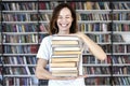 Woman model college student with books at library holds bunch of books, laughs looks smart, smiling to camera