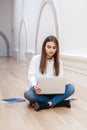 Woman model with long dark hair in white shirt and blue jeans sitting on floor in hall at college university working on laptop
