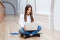 Woman model with long dark hair in white shirt and blue jeans sitting on floor in hall at college university working on laptop