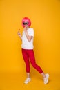 Woman model in the yellow studio with lollipop in a pink wig and bright clothes. Royalty Free Stock Photo