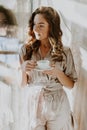 Woman in the morning. Attractive sexy woman with neat body is holding a cup with hot tea or coffee and looking at the sunrise