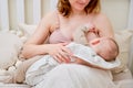 Woman mother breastfeeds infant baby boy sitting on home bed. Mom feeds milk toddler child in the bedroom Royalty Free Stock Photo