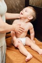 Woman mother giving massage to happy toddler baby sitting on brown