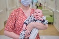 Woman mother in medical face mask holds baby boy in hospital lobby. Mom with child son in her arms visit in the clinic hall Royalty Free Stock Photo