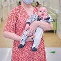 Woman mother in medical face mask holds baby boy in hospital lobby. Mom with child son in her arms visit in the clinic hall Royalty Free Stock Photo