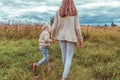 Woman mother walks field, holds hand of little boy son, autumn city, walk in park, background grass, warm casual clothes Royalty Free Stock Photo