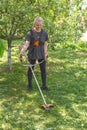 A woman mows grass on his property with a gasoline trimmer