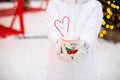 Woman with mug with snow, candy cane and inscription Merry and Bright in her hands outdoor in warm clothes in winter festive