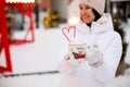 Woman with mug with snow, candy cane and inscription Merry and Bright in her hands outdoor in warm clothes in winter festive