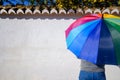 Woman with multicolored open umbrella in front of a white background wall on a sunny day Royalty Free Stock Photo