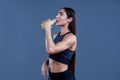 Woman with muscular body in sports clothing with orange juice after workout on grey background. Image with space for text.