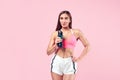 Woman with muscular body in sports clothing relaxing after workout, drinking water on pink background. Image with space for text.