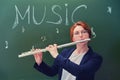 Woman music teacher plays the flute at the blackboard, copy space. Cute school teacher on green background, close up