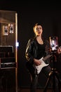 Woman musician playing at electric guitar while recording heavy metal song on phone