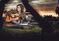 woman musician plays her guitar in a park while people pass by indifferently in front of her