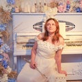 Woman musician sits with a flute on the background of a piano decorated with flowers