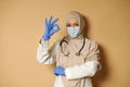 Beautiful Muslim doctor in medical mask covered head in hijab posing on beige background with copy space and gesturing OK with her