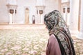 Woman in Muslim prayer room in mosque. Young lady wearing headscarf. Traditional carpet and Arab architecture.