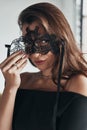 Woman is a mystery. Attractive young woman in elegant black dress wearing a black mask while standing in the room