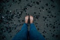 Woman naked feet with blue jeans on black sand and stones top view Royalty Free Stock Photo