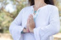 Woman in namaste gesture close up, practicing yoga and meditation outdoors. White clothing with boho chic jewelry.