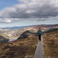 Woman on a narrow boardwalk against the background of mountains. Glendalough, Wicklow, Ireland.