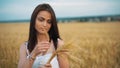 The woman in a national white shirt holds in hand the ripened wheat ears on a gold field background. harvest