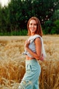 A woman in natural clothes with a string bag made of eco-mesh, fruits, apples is walking along a path in a wheat field Royalty Free Stock Photo