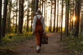 Woman naturalist in orange overalls with backpack on ecological hiking trail in forest Royalty Free Stock Photo