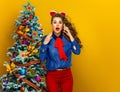 Woman near Christmas tree on yellow background using cell phone Royalty Free Stock Photo