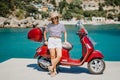 Woman near retro styled scooter motor bike in candy apple red color, pier in luxury resort. Amazing turquoise sea water Royalty Free Stock Photo