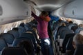 Woman placing suitcase inside overhead compartment in plane